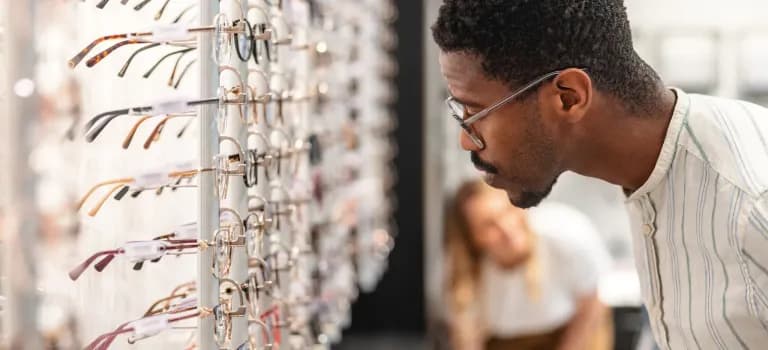 Man examining eyeglass frames from display wall at boutique optical shop